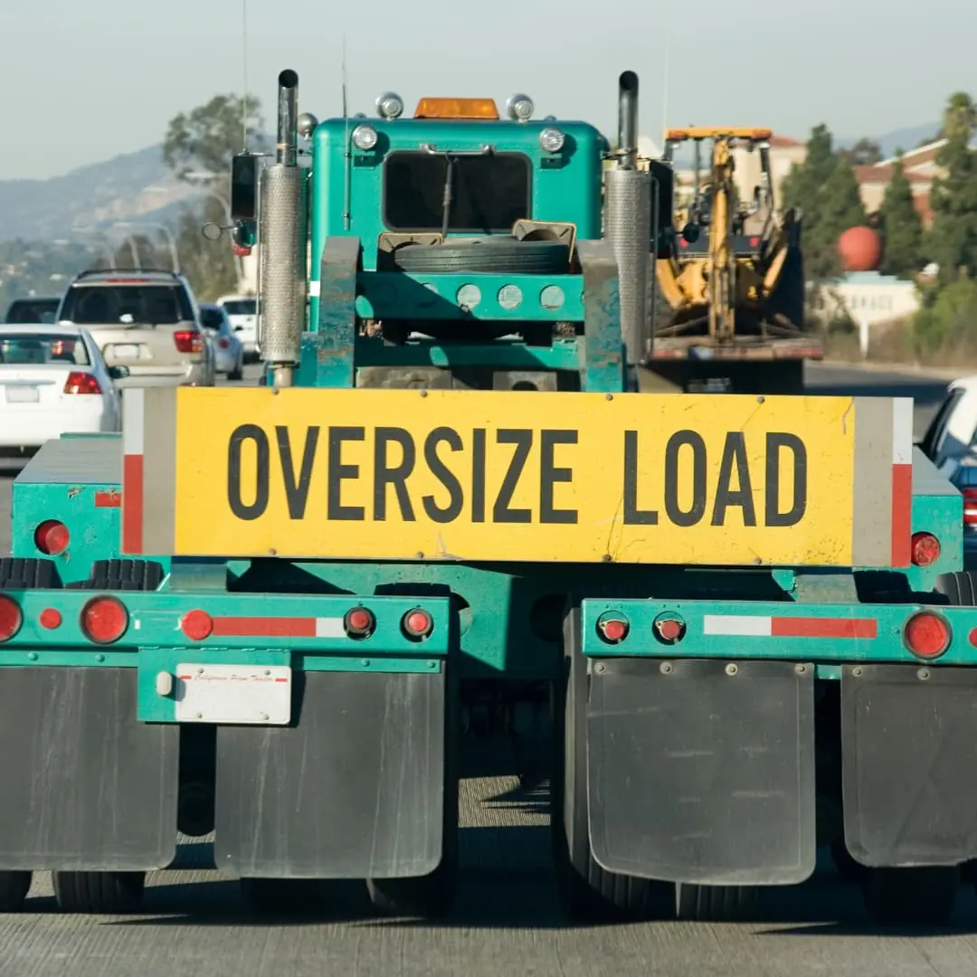 a behind view of a turquois semi truck with a yellow and black Oversize Load sign