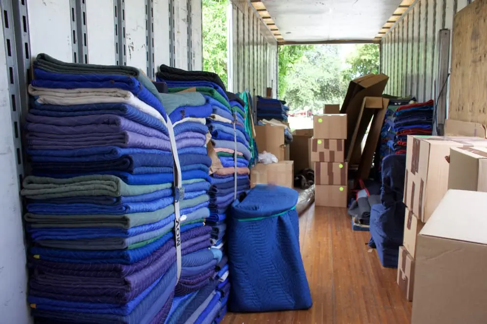 Moving and storage trailer with strapped moving blankets and packed boxes on floor