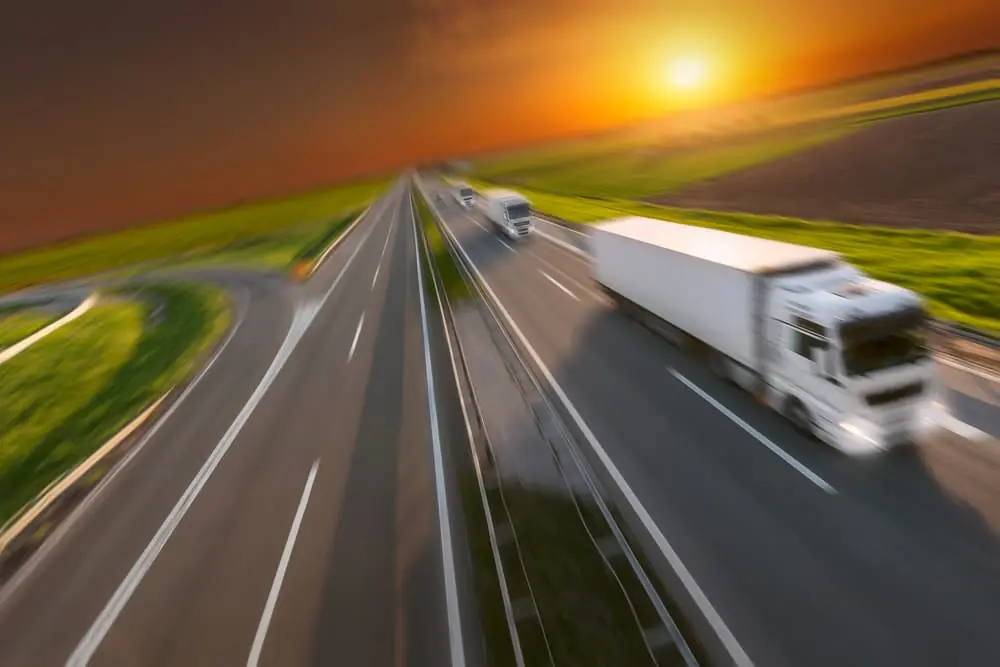 Three new expedited trucks in a row at left side driving on freeway with speed blurred motion