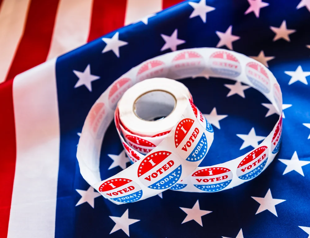 Campaign Shipping-roll-of-vote-now-stickers-on-top-of-american-flag