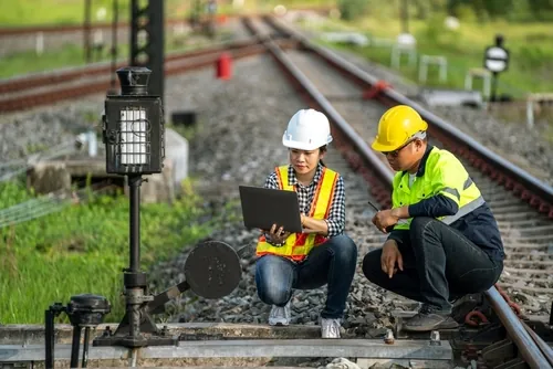 two railroad workers looking at at tablet on train tracks