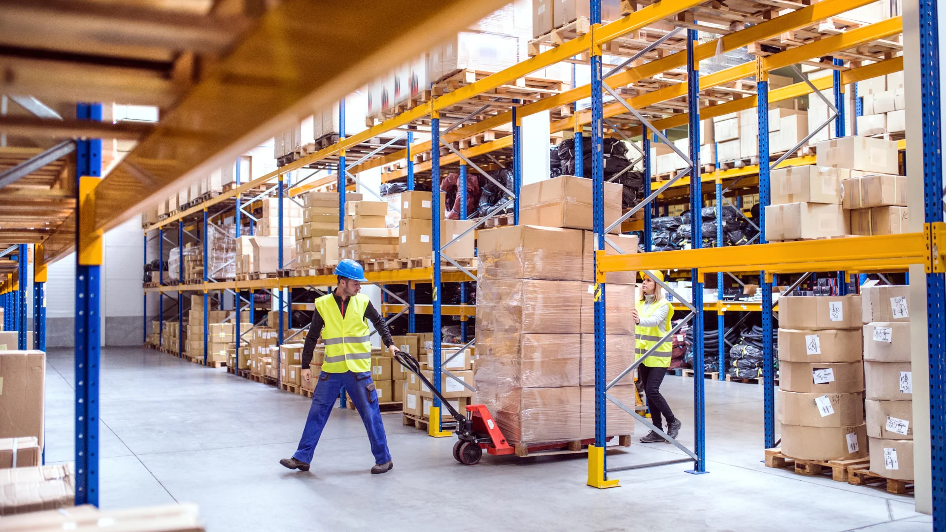 workers pulling shrink wrapped palletized boxes through warehouse aisles