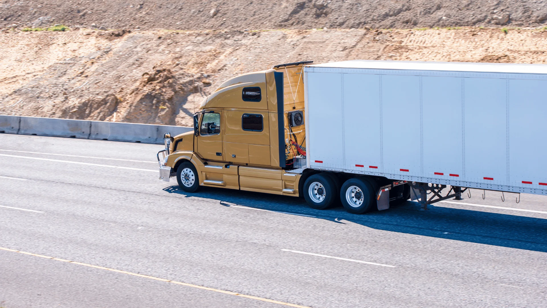 LTL Freight Tariffs gold semi truck driving down highway past cliffside during the day