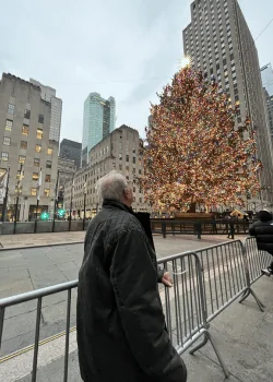 An older gentleman looks up at the lit Rockefeller Christmas tree from across the street.