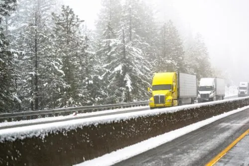 semi truck with yellow cab driving on a snowy highway 