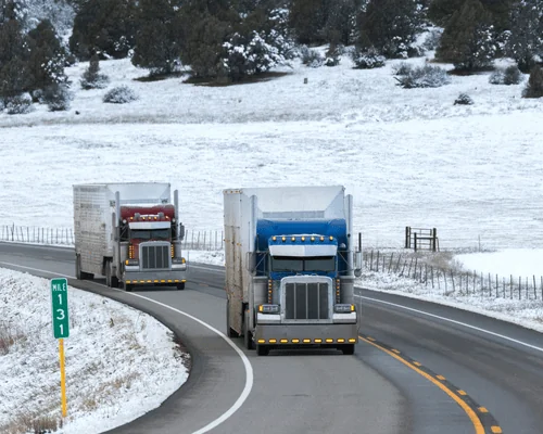 two trucks driving down snowy highway