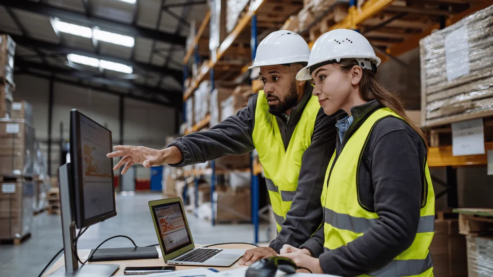 Freight Management Company two warehouse workers analyzing data on laptop and computer