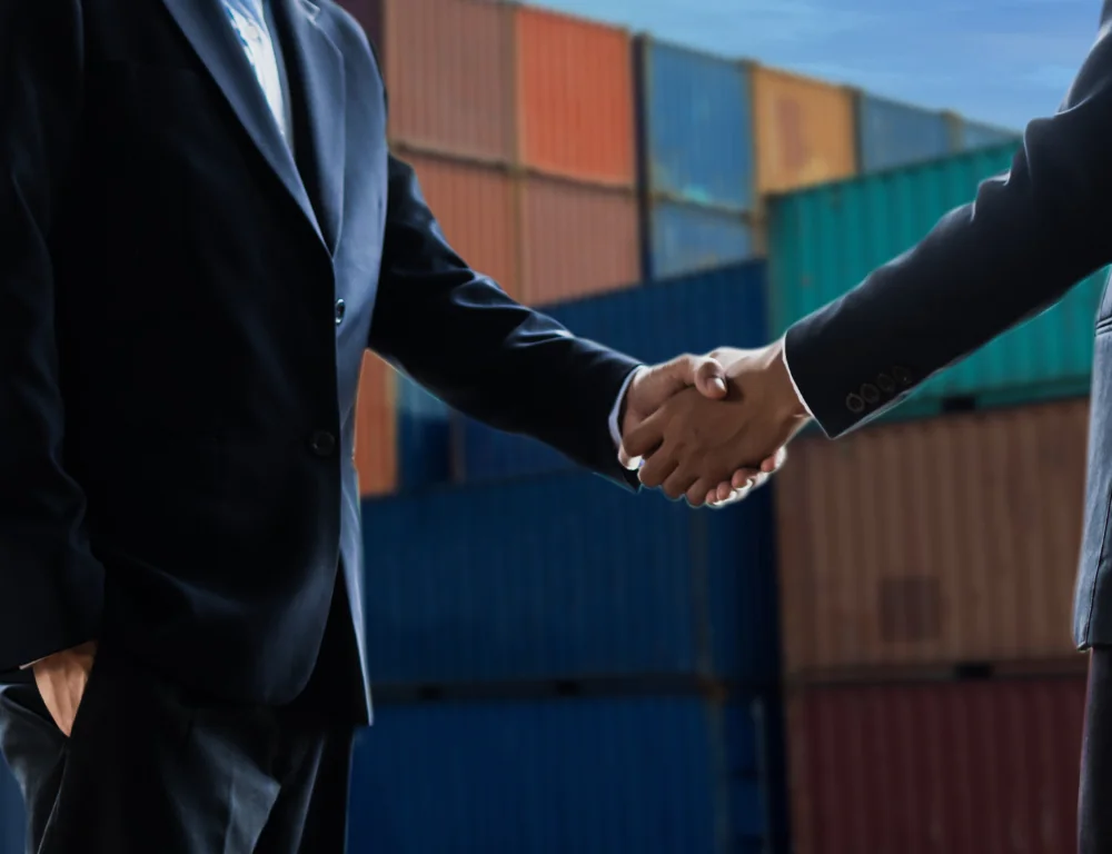 two business men shaking hands in front of shipping containers