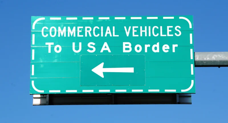 green and white commercial vehicles to usa border sign