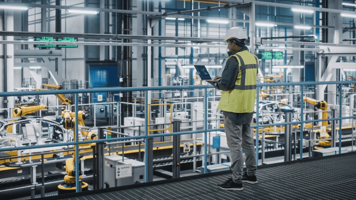 car factory engineer in high visibility vest on laptop overseeing production in automotive manufacturing plant