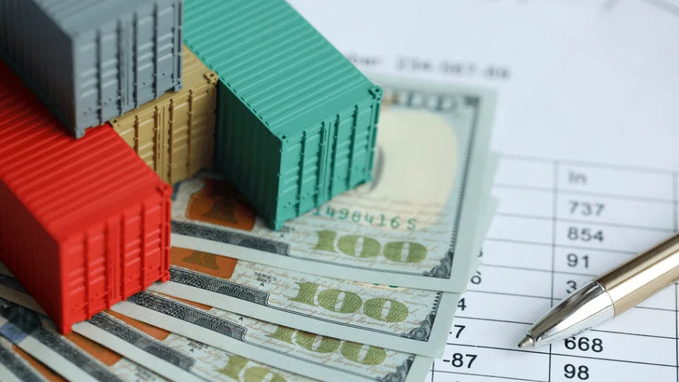 Reducing Freight Costs for Enterprises a stack of toy shipping containers on top of $100 bills and invoice data table