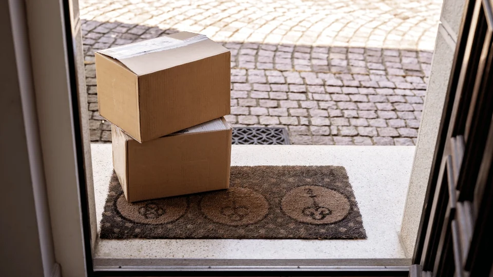 two cardboard box packages on top of welcome mat in front of open door