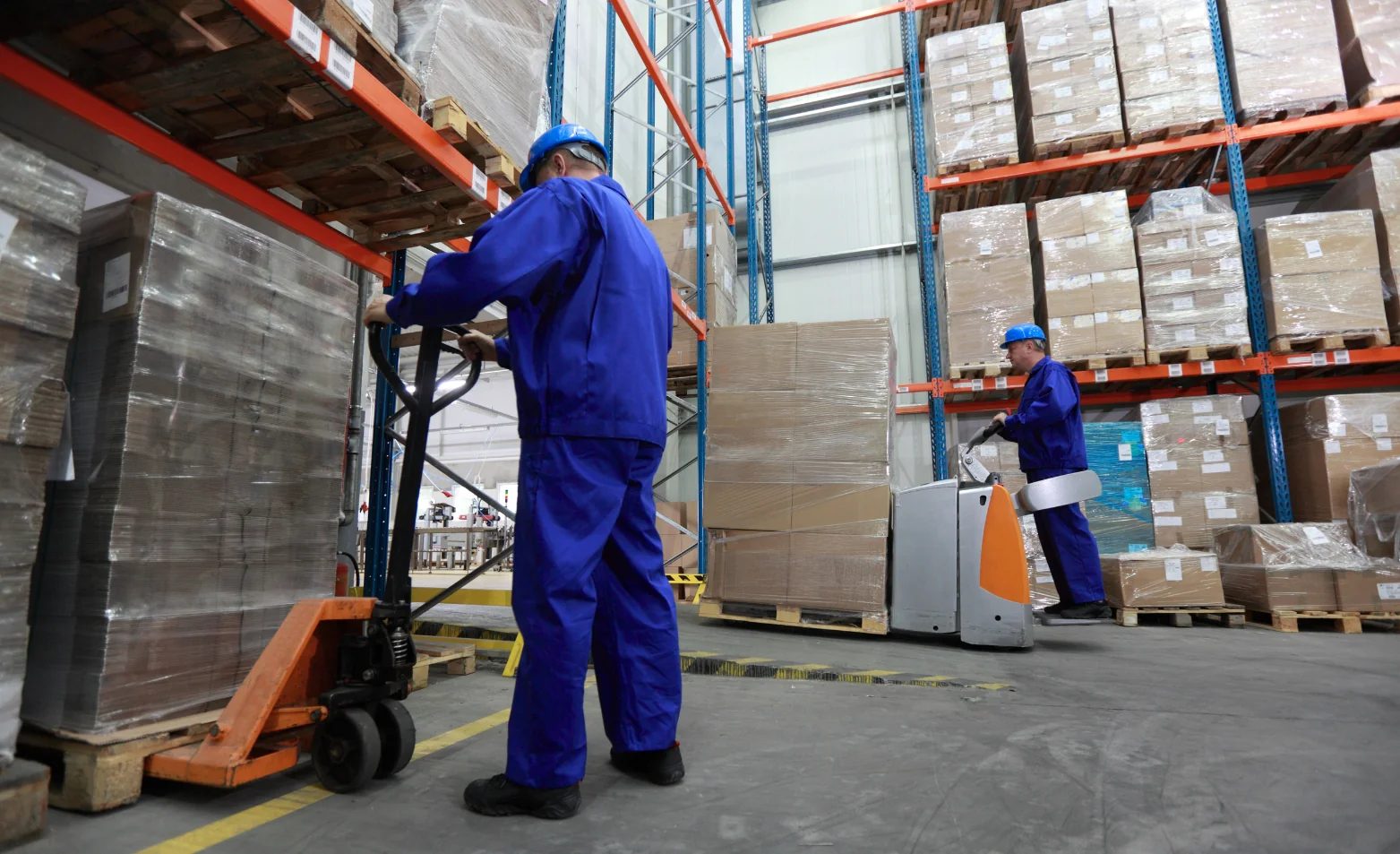 two warehouse workers operating a pallet jacks