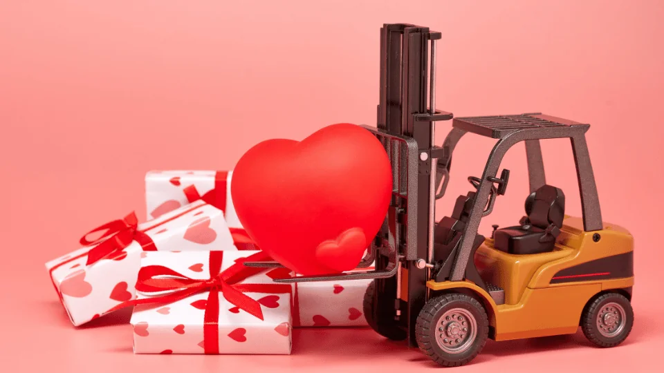 toy forklift holding red heart next to pile of white gift boxes wrapped in red strings