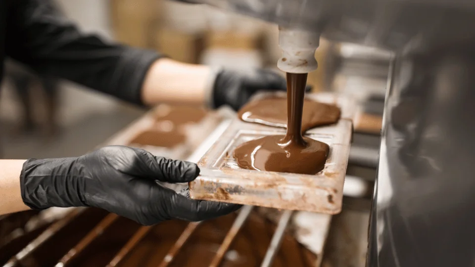 worker pouring liquid chocolate over a mold