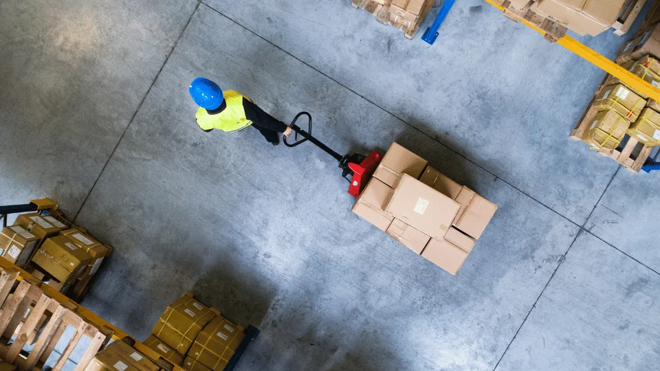 top view of warehouse worker pulling pallet of boxes on pallet jack