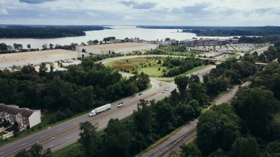 aerial view of semi trucks driving down highway with distribution center in the distance