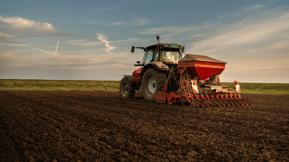 plow tractor being driven by farmer through soil during sunset