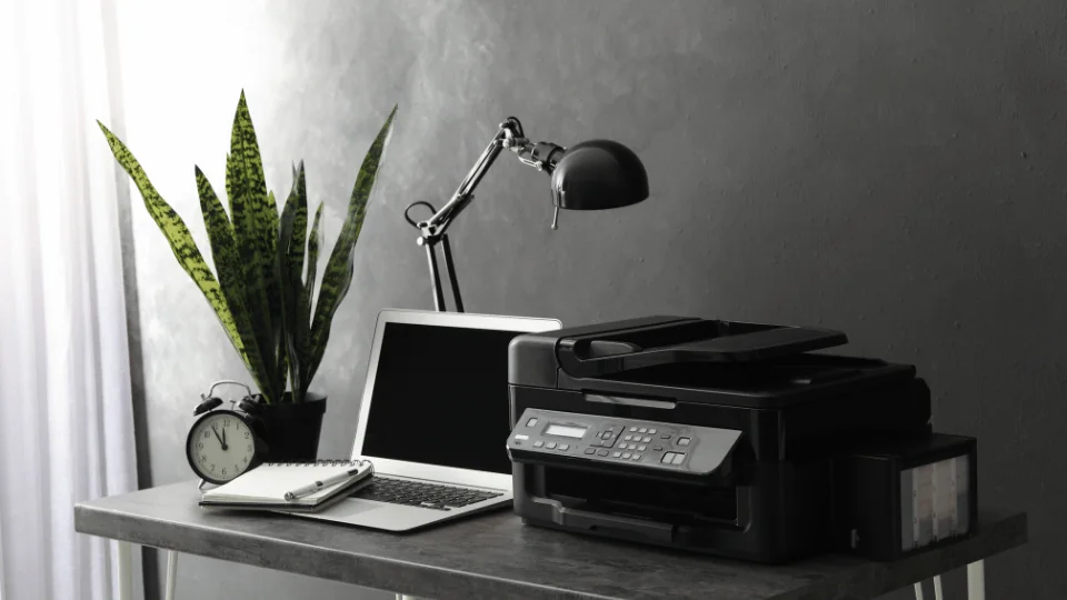 Shipping Office Supplies and Equipment modern desk set up with laptop, black printer, black lamp, a notepad, an analog alarm clock, and a potted plant